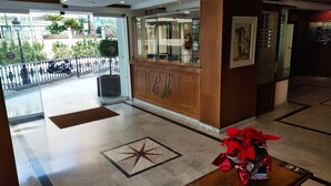 A hotel lobby with a reception desk, a glass door leading outside, and a star-patterned floor design.