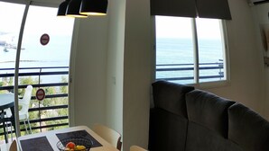 A dining area with a table set for two, a cushioned bench, and a view of the sea through large windows.