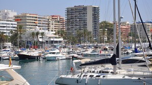 A marina with various boats docked, surrounded by buildings and palm trees.