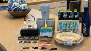 A kitchen counter with a bowl of towels, a kettle, a coffee maker, a bottle of water, a box of beer, a bottle of wine, and a pie. - Sunset Villas: Bayfront Beach Compound<br>**28 Night Min** (Key Largo)