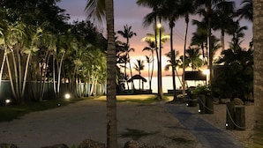 A paved pathway curving through a landscaped area with palm trees and a sunset in the background. - Sunset Villas: Bayfront Beach Compound<br>**28 Night Min** (Key Largo)