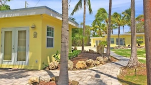 A yellow building with a paved walkway, palm trees, and a clear sky. - Sunset Villas: Bayfront Beach Compound<br>**28 Night Min** (Key Largo)