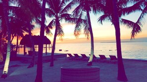 Relax on the beach with a thatched-roof hut and lounge chairs.