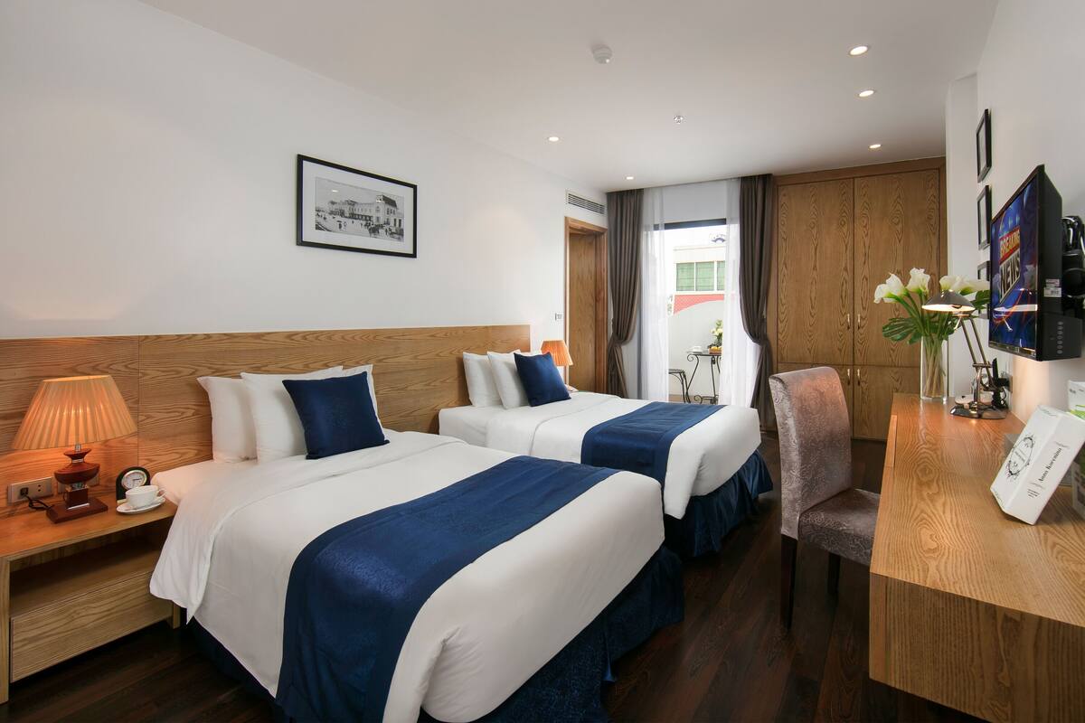 Habitación de hotel con dos camas, un escritorio, una silla, un televisor y un cuadro en la pared.