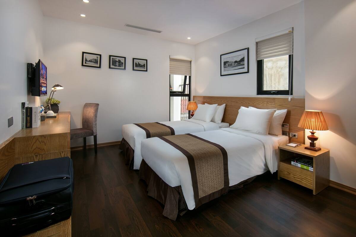 Habitación de hotel con dos camas, un escritorio, una silla, un televisor y una lámpara.