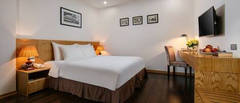 A neatly arranged hotel room with a wooden bed, bedside lamps, a desk with a chair, and a flat-screen TV mounted on the wall.
