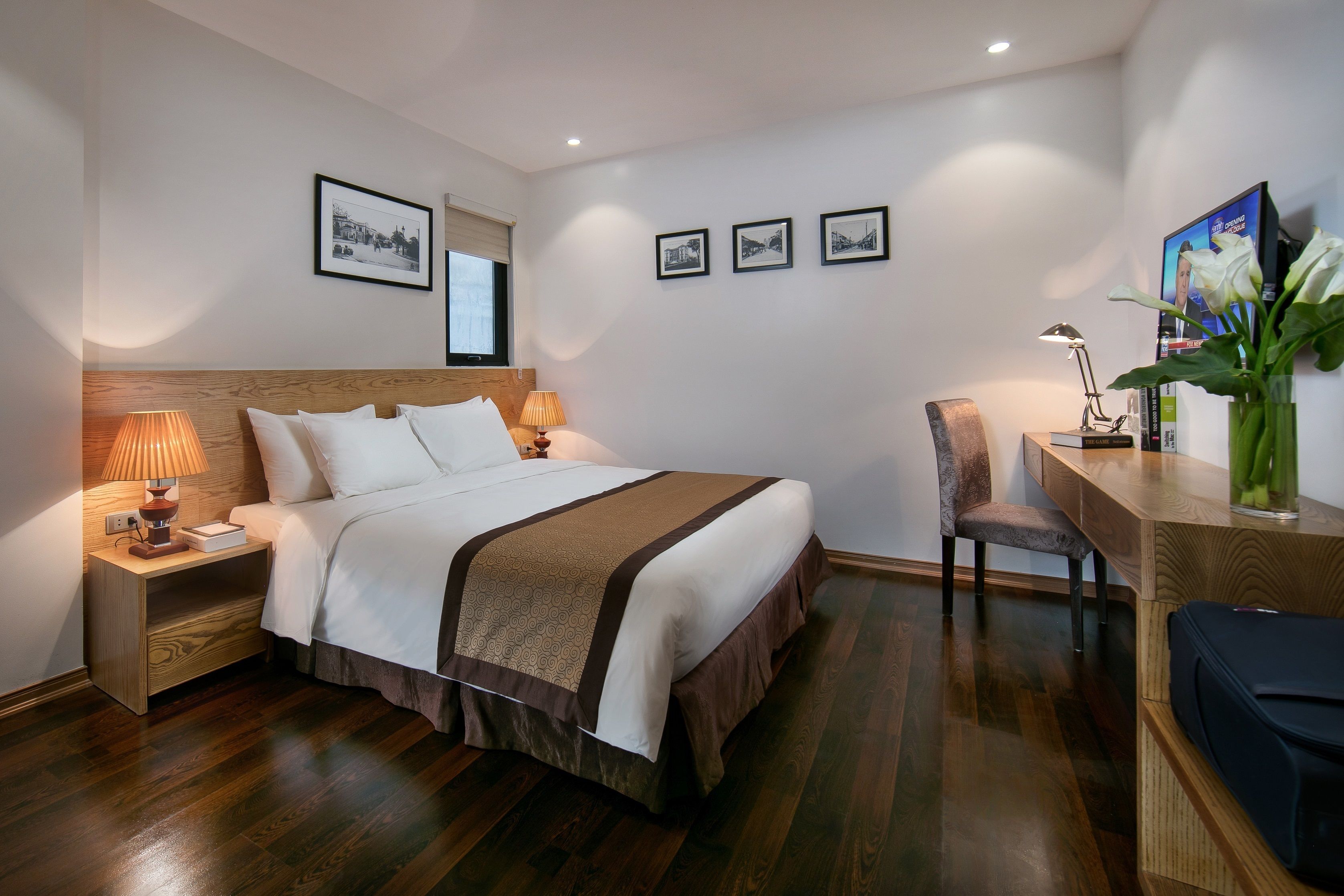 A neatly arranged hotel room with a bed, bedside lamps, a desk with a chair, and a television.