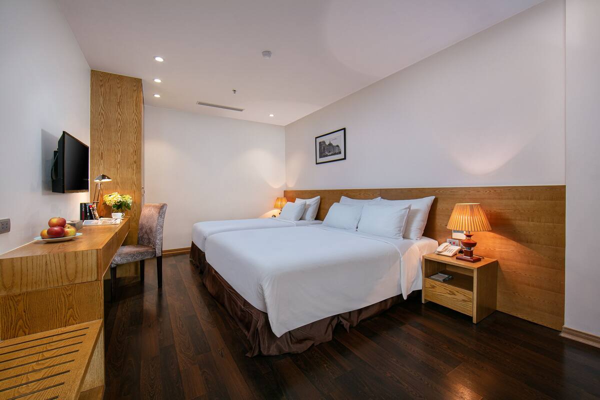 Una habitación de hotel moderna con una cama grande, mesitas de noche, un escritorio con una silla, un televisor de pantalla plana y un cuadro en la pared.