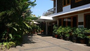 Un patio con plantas en macetas, una zona de estar cubierta y un edificio con amplios ventanales y un balcón.