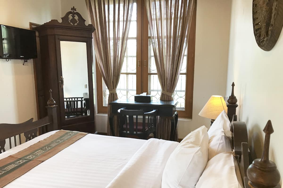 A hotel room with a large bed, a desk, a chair, a television, and curtains.
