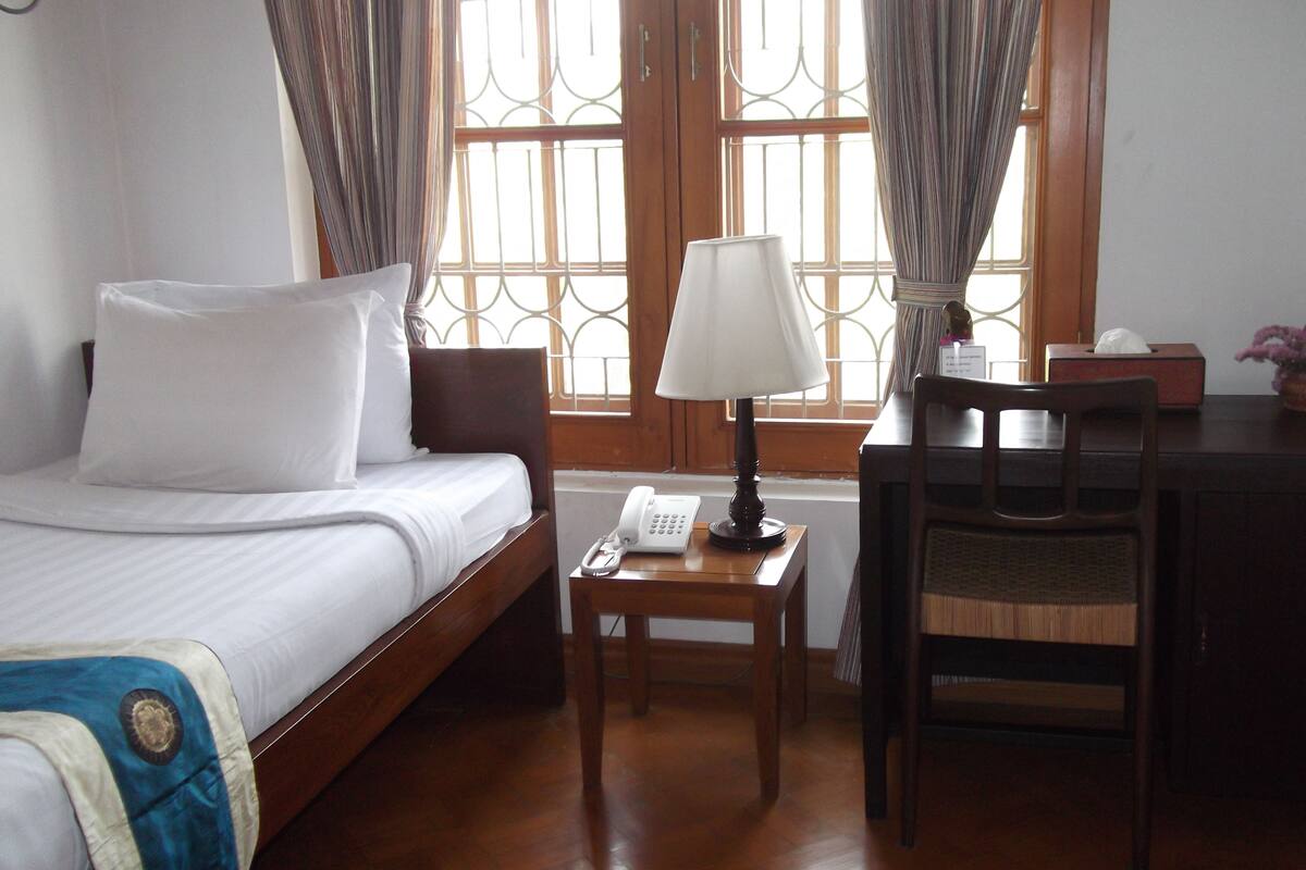 A hotel room with a bed, a desk with a lamp, a telephone, and a chair.