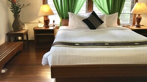 Una cama bien hecha con sábanas blancas y un almohadón negro con diseño geométrico. Hay dos lámparas de noche en mesitas de madera, y una planta en maceta al lado izquierdo de la cama.
