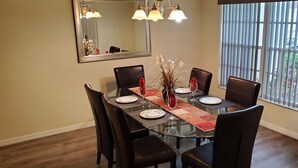 A dining area with a glass table, dark chairs, a red table runner, and a vase with dried plants. - Executive Home with Pool, Spa & Games Room minutes to Disney World (Davenport)