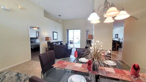 A dining area with a glass table set for four, surrounded by dark leather chairs. A decorative vase with long, thin branches is placed in the center. - Executive Home with Pool, Spa & Games Room minutes to Disney World (Davenport)