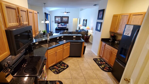 A kitchen with wooden cabinets, a black stove, and a refrigerator. - Executive Home with Pool, Spa & Games Room minutes to Disney World (Davenport)