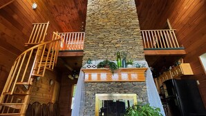 A wooden interior with a stone fireplace, wooden staircase, and a kitchen area.