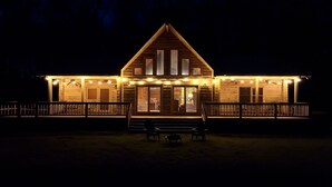 A log cabin with a porch, string lights, and a bench.