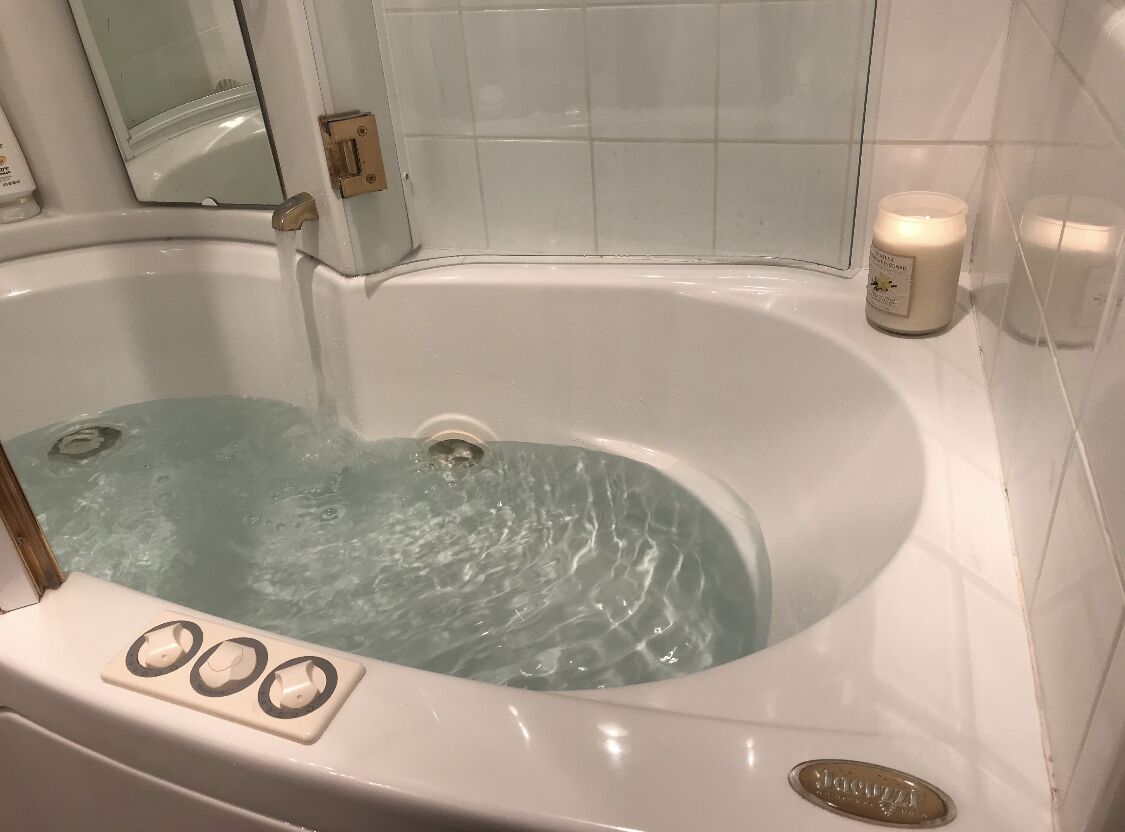A bathtub with water running, a control panel with temperature settings, and two candles on the wall.