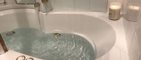 A bathtub with water running, a control panel with temperature settings, and two candles on the wall.