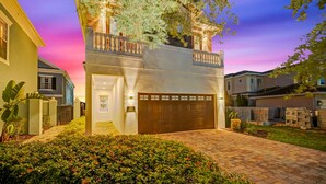 A modern two-story house with a well-lit garage, surrounded by a landscaped garden and a clear view of the sky.