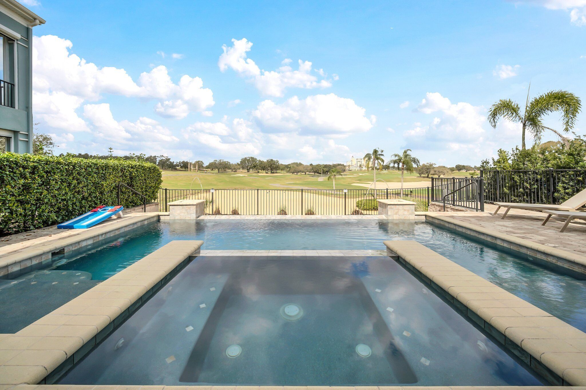 Una piscina con vistas a un campo de golf, un área de descanso con sillas y una palmera.