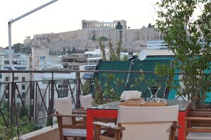 A terrace with outdoor seating, a view of ancient ruins in the background, and a modern building in the foreground. - Acropolis Home (Athens)