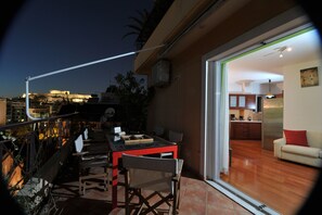 A balcony with a dining area, a sliding glass door leading to a living room with a sofa and a kitchen visible inside. - Acropolis Home (Athens)