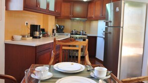 A kitchen with wooden cabinets, a stainless steel refrigerator, and a dining table set with plates, cups, and a pitcher. - Acropolis Home (Athens)