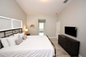 A bedroom with a bed, a dresser, a TV, and a door leading to a balcony.