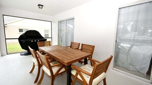 Un espace repas avec une table et des chaises en bois, un barbecue et de grandes fenêtres.