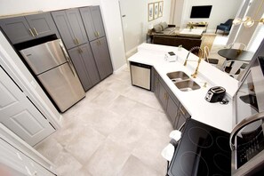 A modern kitchen with stainless steel appliances, a white countertop, and a dining area with a sofa and table. - Updated 5BR Private Pool Home | Quiet Community | BBQ | Dog Friendly (Clermont)