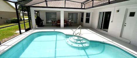 A covered swimming pool with a patio area, a door, and a window.