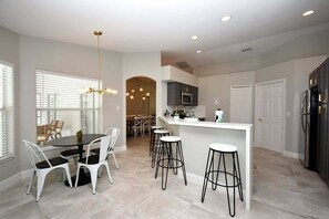 A modern kitchen with a central island, bar stools, and a dining area with chairs.
