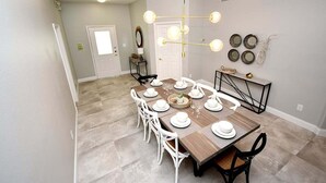 A dining area with a wooden table set for six, white chairs, and a chandelier.