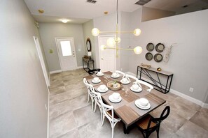 A dining area with a wooden table set for six, white chairs, and a chandelier. - Updated 5BR Private Pool Home | Quiet Community | BBQ | Dog Friendly (Clermont)