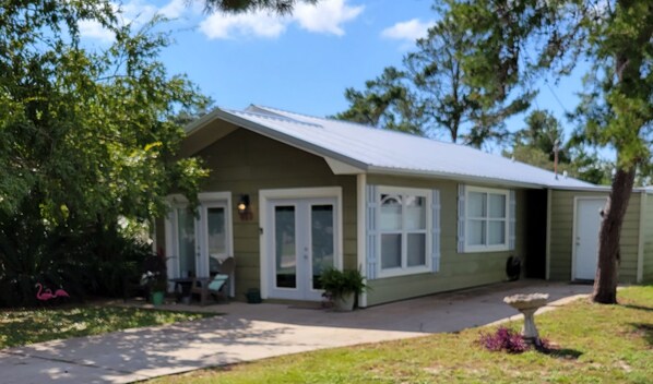 A single-story house with a front porch, a small garden, and a clear sky.