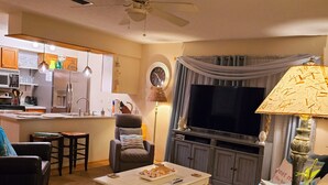 A living room with a sofa, coffee table, and a TV. There is a kitchen area with appliances and a dining table. - A Special Getaway! (Panama City Beach)