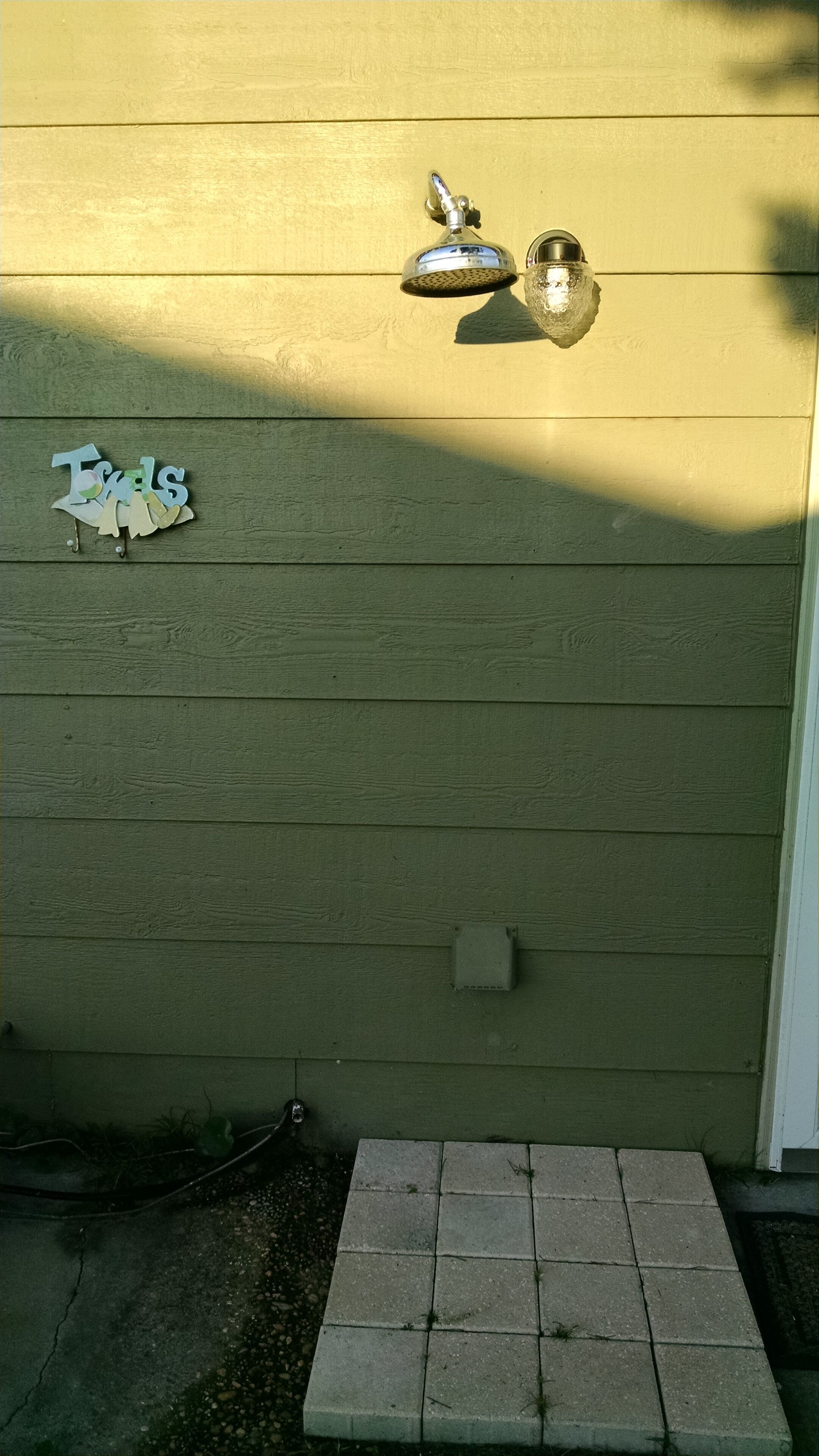 A wooden exterior wall with a metal doorbell, a mailbox, and a small electrical box.