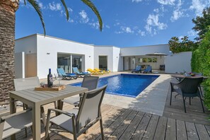 Uma área moderna de piscina ao ar livre com um deck de madeira, espreguiçadeiras e uma mesa de jantar.