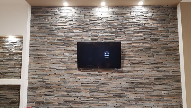 A modern living room with a stone wall and a flat-screen TV mounted on it.