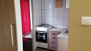 A compact kitchen with white tiled walls, a gas stove, a built-in oven, and a sink.