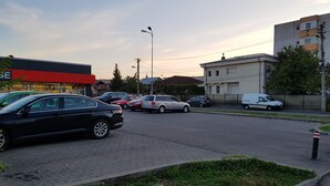 A parking lot with several cars, a building with a red and white facade, and a white van parked on the side.