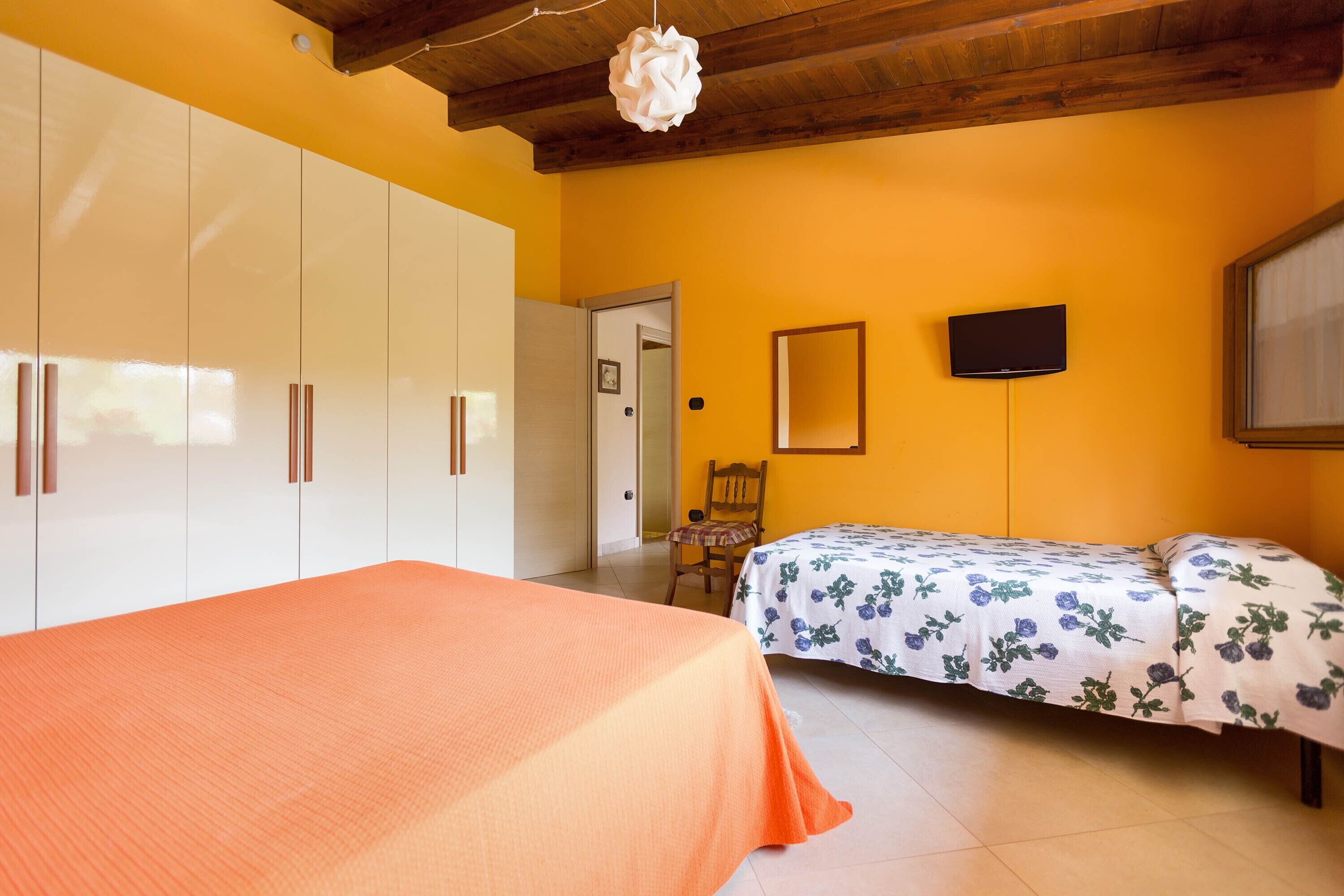 Ein Schlafzimmer mit einem Bett, einem Sessel, einem Kleiderschrank, einem Fernseher und einer Tür.