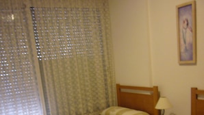 Una habitación de hotel con dos camas individuales, una mesita de noche con lámpara y una ventana con cortinas.