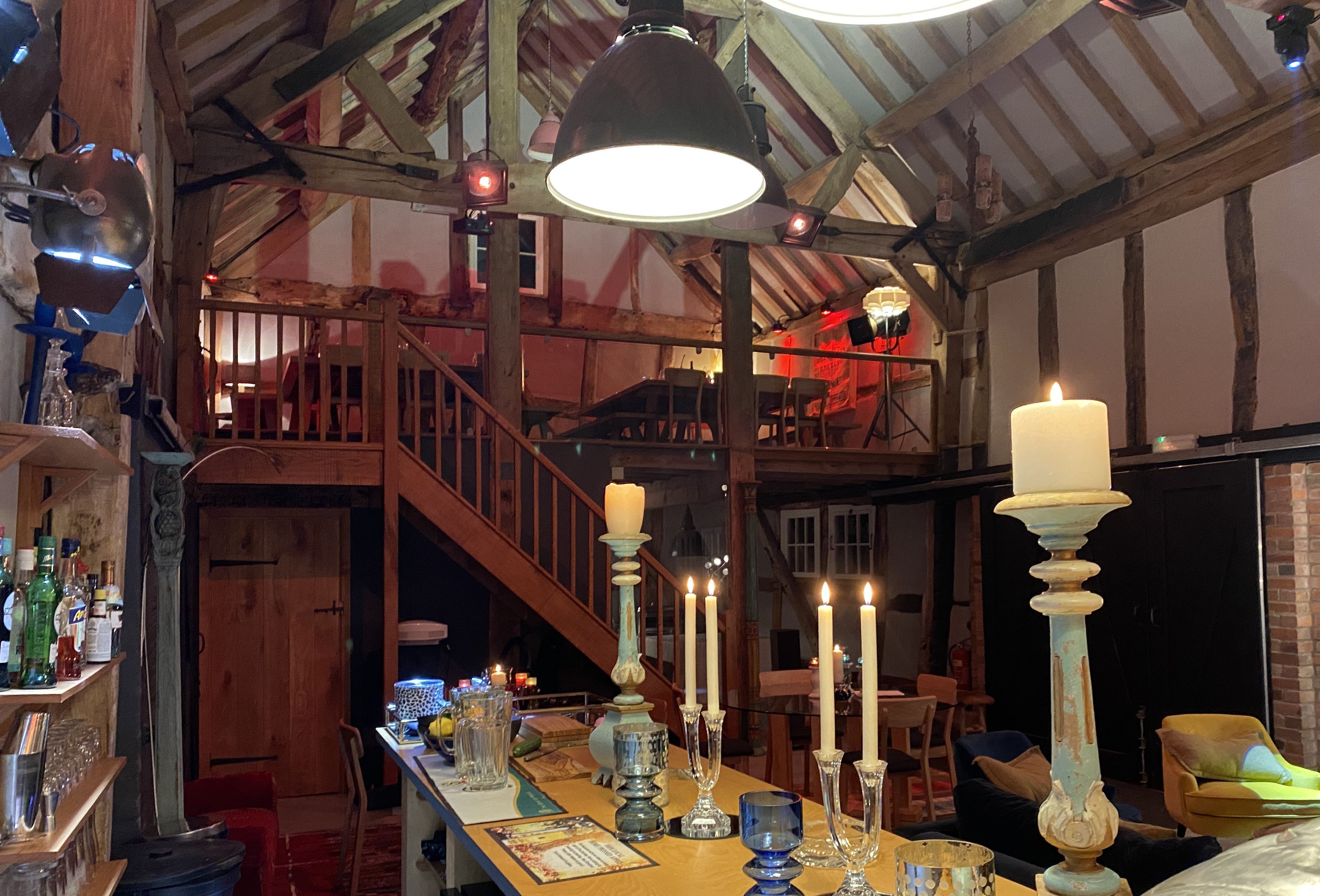 Un interior rústico con una escalera de madera, una zona de bar con botellas y vasos, y una mesa con velas y adornos.