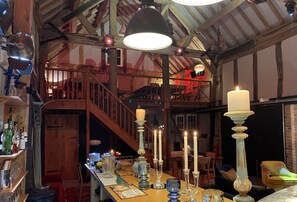 A rustic interior with a wooden staircase, a bar area with bottles and glasses, and a table with candles and decorative items.