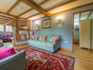 A cozy living room with a blue sofa, colorful pillows, a patterned rug, and wooden beams on the ceiling.
