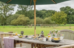 An outdoor dining area with a wooden table set for breakfast, surrounded by chairs and an umbrella.