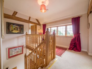 A staircase with wooden balusters leading to an upper floor, a red curtain on a window, and a painting on the wall.