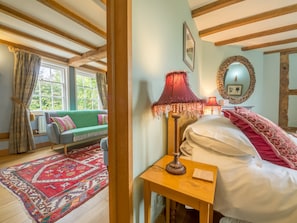 Um quarto aconchegante com uma cama, um sofá verde, um tapete vermelho estampado e uma mesa de madeira com uma luminária.